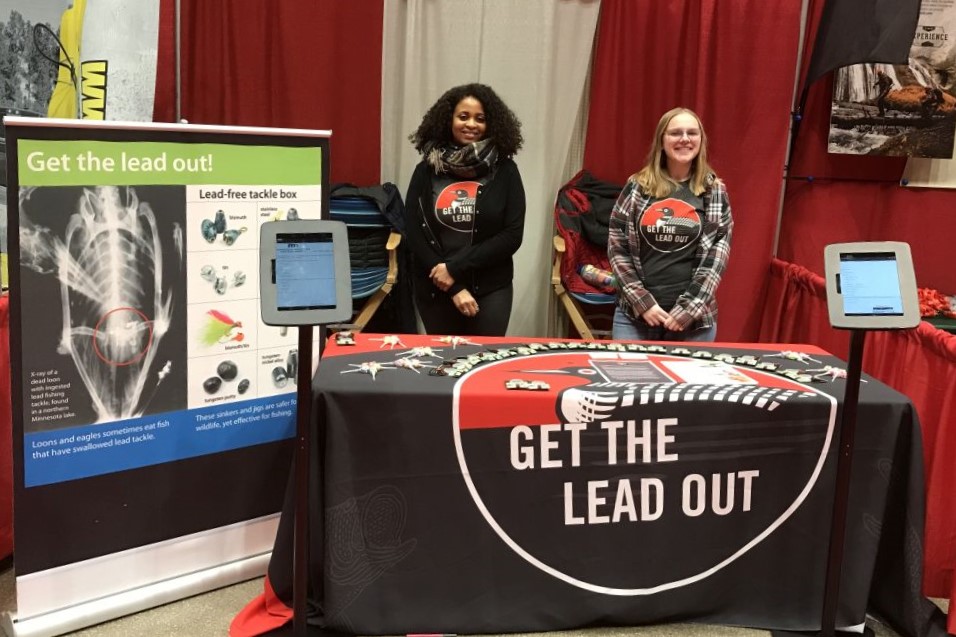 Two "Get the Lead Out" outreach team members in front of a trade show booth.